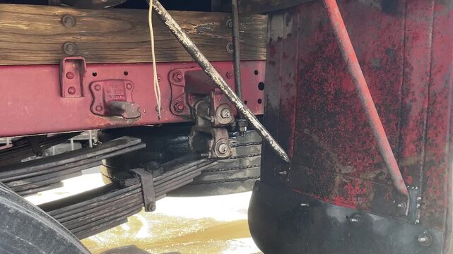 High pressure water sprays beneath a red truck, cleaning the undercarriage, suspension, and metal components while removing dirt and grime during an outdoor automobile washing process today.