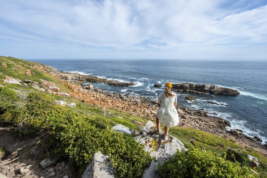 Young pretty woman wearing dress off coast and sea at Robberg Nature Reserve, Plettenberg Bay, South Africa