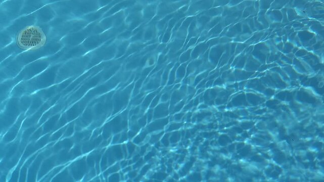 Clear blue swimming pool water rippling in the sun with caustic light reflections at the bottom of the pool