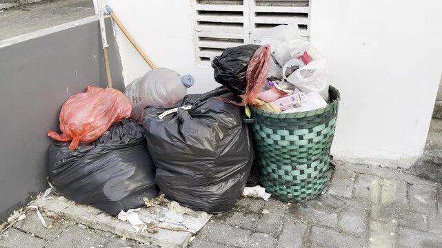 Overflowing trash bin with plastic bags and household waste outdoors