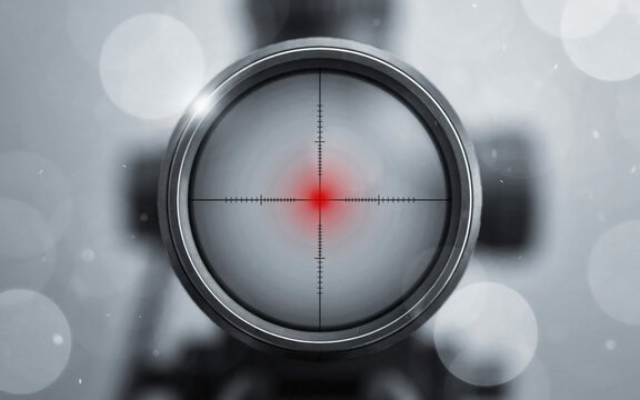 Sniper rifle scope showing a bright red illuminated dot in the center of the black crosshair reticle with a blurred metallic gray background reflecting soft light during a cold day.
