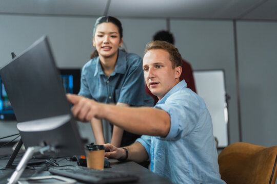Man developer points at his monitor to walk a woman colleague through the software he is building, showing steady project progress in a modern tech office.