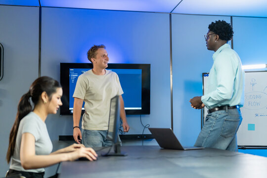 Diverse developer team engages in casual discussion around coding workflow planning, sharing ideas and collaborative insights for development process optimization.