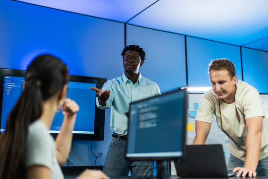 African male developer leads code architecture discussion with diverse team members, explaining technical solutions and design concepts through interactive dialogue.
