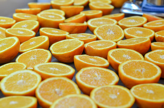 A large number of fresh orange halves and slices laid out neatly in rows, consistent with preparation for juicing, drying, or candying.