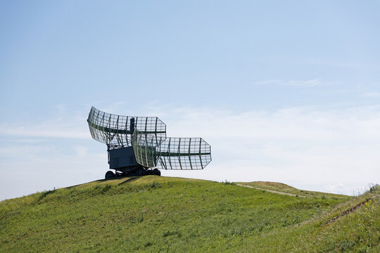 Military Radar Station on Top of a Green Hill, with its Antenna Pointed Skyward Against Clear Blue Sky
