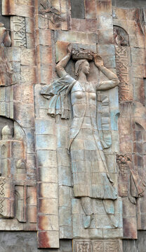 A detailed Soviet-era bas-relief sculpture carved into a stone wall depicts a traditional woman carrying a vessel atop her head in Osh, Kyrgyzstan