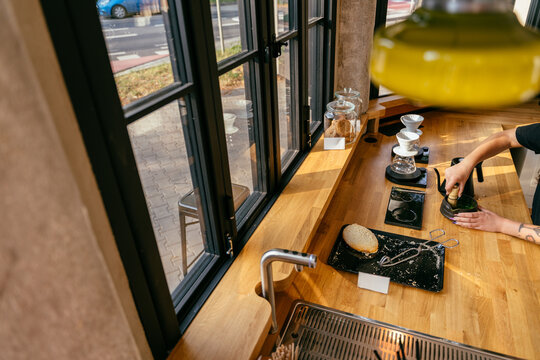 Modern specialty cafe counter with barista preparing matcha beside large industrial style windows