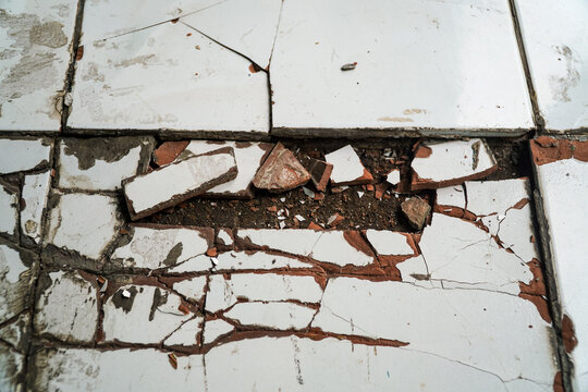 Cracked white tiles with broken pieces scattered across a damaged floor surface showing exposed mortar and debris, ideal for construction, renovation or decay themes.