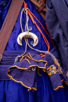 A close-up of a necklace adorned with a moon-shaped pendant, worn over a traditional blue and purple embroidered Sikh garment in Amritsar, India.