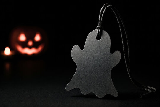 Blank Ghost Shaped Price Tag with Glowing Jack O Lantern in Dark Halloween Background