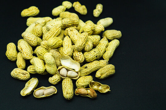 Peanuts in shells and cracked open rest on a black background. Some nuts show inner white seeds clearly. Texture of shells appears rough and natural. No people, so no emotions are present.