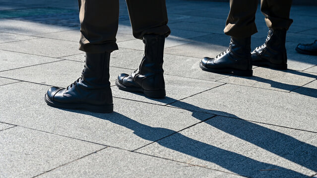 A formation of soldiers wearing camouflage trousers and black combat boots standing in a neat line during a military drill. A row of military personnel dressed in matching tactical camouflage uniform.