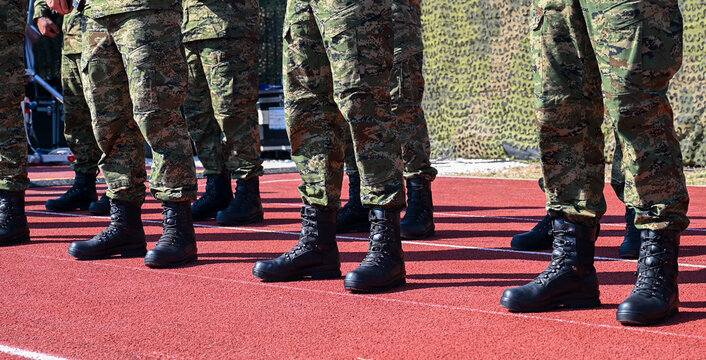 A formation of soldiers wearing camouflage trousers and black combat boots standing in a neat line during a military drill. A row of military personnel dressed in matching tactical camouflage uniform.