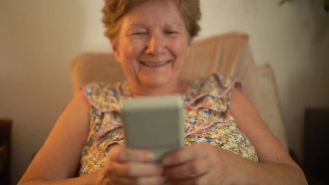 A retired senior woman at home playing a portable video retro game console and having fun