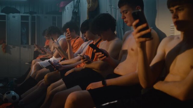 Football Team Everyday Routine after Training. Players Unwind in Locker Room, Quietly Using Smartphones while Recovering From Exercise, Genuine Moments of Friendship, Discipline, Athletic Lifestyle.