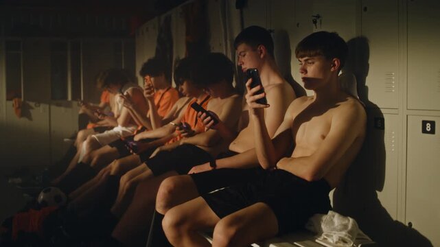 Football Teammates Sharing Calm Moment in Locker Room after Demanding Training Session. Players Recover Physically while Checking Smartphones. Daily Routine of Young Athletes, Connected Lifestyles.