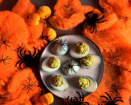 Halloween deviled eggs stuffed with avocado guacamole cream on a plate decorated with black spiders and orange cobwebs for spooky holiday party food