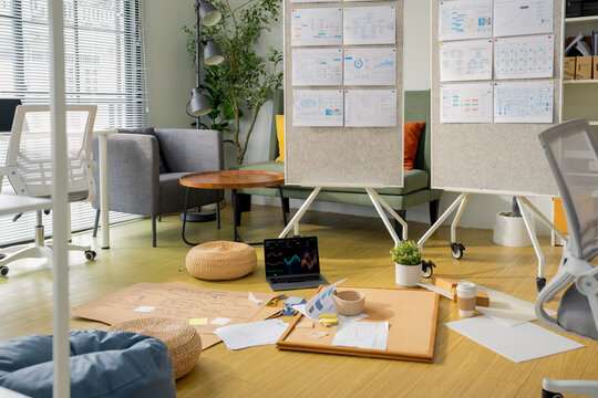A creative workspace floor scattered with mind-map sketches, a laptop showing stock charts, and mood boards pinned to whiteboards a candid glimpse into a startup's collaborative brainstorming session.