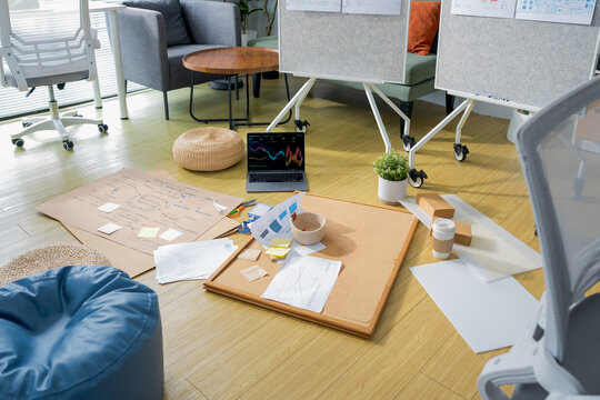 A creative workspace floor scattered with mind-map sketches, a laptop showing stock charts, and mood boards pinned to whiteboards a candid glimpse into a startup's collaborative brainstorming session.