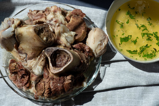 Boiled beef shank pieces with bone marrow served with bowl of homemade collagen-rich bone broth. Traditional hearty soup.
