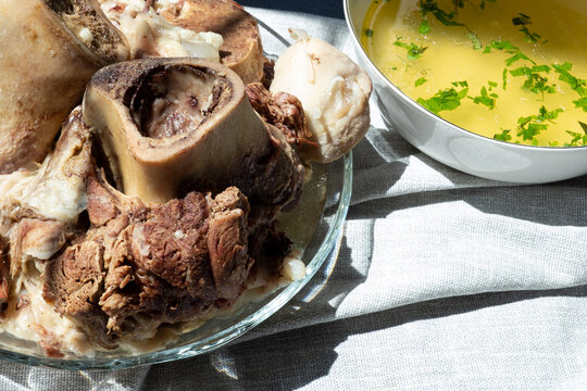 Boiled beef shank pieces with bone marrow served with bowl of homemade collagen-rich bone broth. Traditional hearty soup.