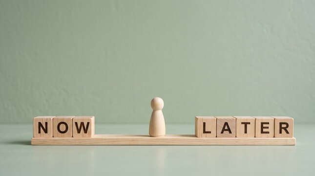 Wooden blocks spelling now and later separated by a pawn figure on a balance scale, symbolizing the of time management, decision making, procrastination versus immediate action