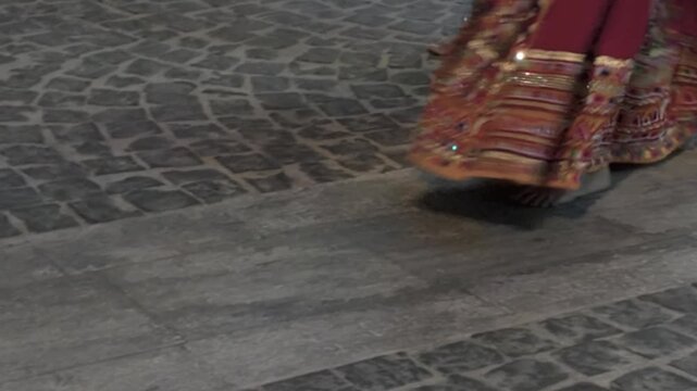 Barefoot people and individuals wearing sandals walk along a grey cobblestone street dressed in vibrant embroidered garments. Such rich cultural expressions celebrate traditional folklore and communit