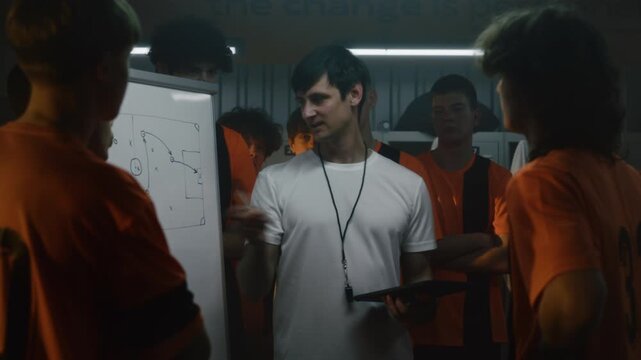 Experienced Soccer Trainer Teaching Game Intelligence and Decision Making Through Visual Tactical Instruction in Locker Room. Football Education, Player Development and Competitive Preparation.