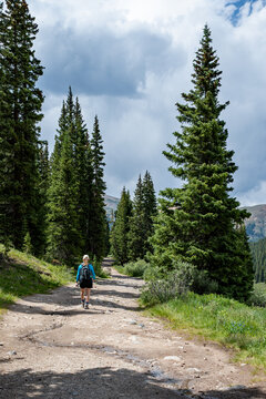 Woman hiking on Mayflower Gulch Trail near Copper Mountain and Leadville, Colorado under stormy summer cloudscape.