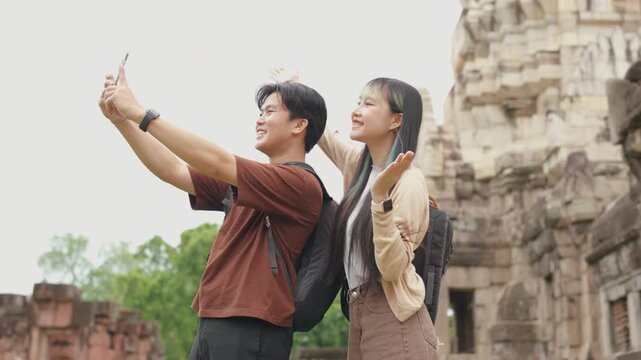 Happy young Asian couple exploring ancient temple ruins with map and smartphone during summer travel vacation. Cheerful romantic tourist lovers enjoying historic sightseeing adventure.