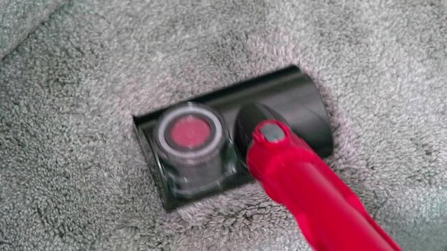 Red vacuum head moves over grey carpet. Carpet fibers lift as cleaning head glides forward. Cleaner's red handle grips firmly for control. No people shown, focus stays on tool and surface