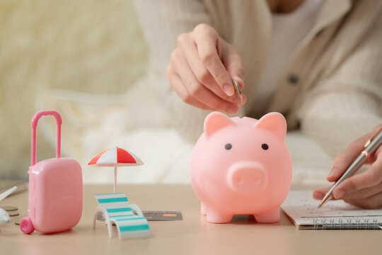 Travel savings and vacation planning concept with a woman putting a coin into a piggy bank beside a suitcase and airplane, saving money for travel, vacation, savings, budget, tourism