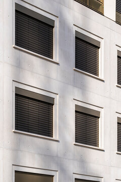 Closed shutters frame windows in a minimal study of architecture, while the urban facade uses repetition and geometry to order the building exterior in daylight.
