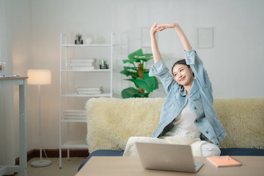 Work break and relaxation concept with a young woman stretching her arms beside a laptop at home, enjoying rest after work, relaxation, stretching, wellness, break, lifestyle