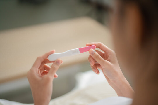 Pregnancy test and reproductive health concept with a woman holding a home test device and checking the result indoors, showing pregnancy, fertility, testing, healthcare, motherhood