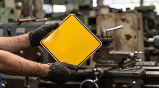 Worker wearing gloves holding an empty yellow square warning sign in a manufacturing factory