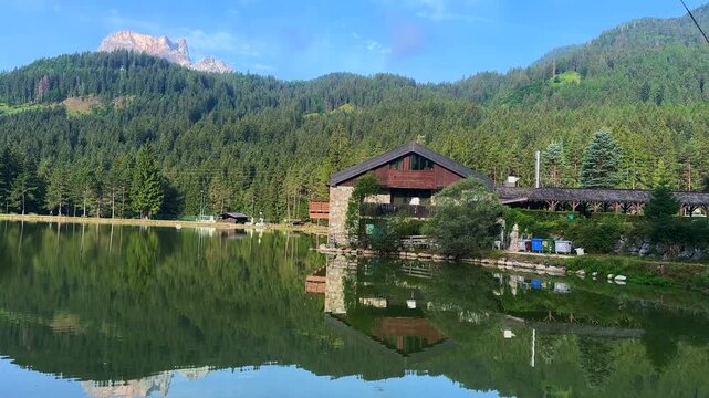 serene lake with a wooden house and mountains in the background, wide-angle shot, static camera position, natural landscape, travel destination, blue and green colors, peaceful and serene.