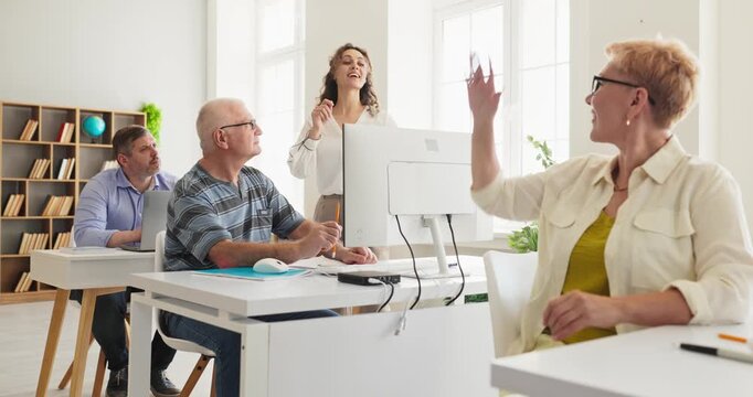 Teacher engages adult students in computer learning. Seniors learn as one raises a hand as the instructor leads training in a classroom promoting education. Clear concept of active learning.