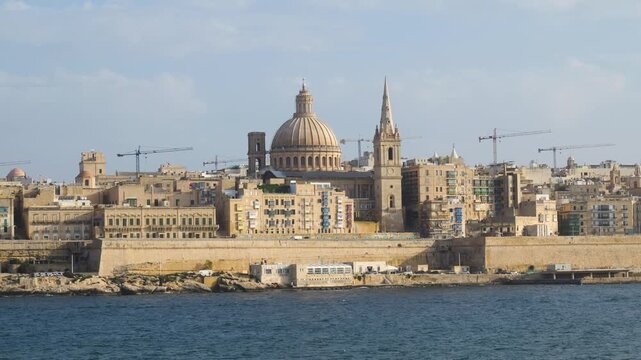 golden hour light bathes the valletta skyline carmelite dome and cathedral spire glowing above the harbour water carmelite church dome st pauls anglican cathedral baroque skyline malta capital city