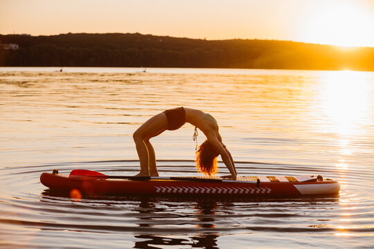 Woman practicing yoga wheel pose on sup at sunset