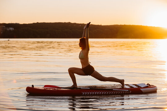 Woman practicing yoga on sup paddleboard at sunset