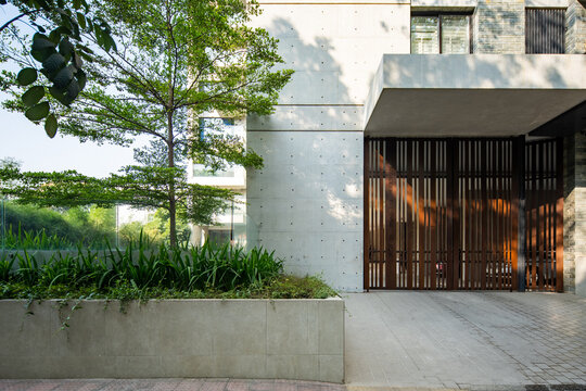 Modern Residential Entrance with Wooden Gate, Concrete Walls, Landscaped Garden, and Tree Shadows