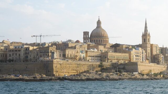 sailboat drifts before the golden hour valletta skyline dome and spire glowing warmly above the calm harbour carmelite church dome st pauls anglican cathedral baroque skyline malta capital city