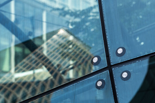Visible hardware anchors an urban building detail as blue glass fills the facade, then reflection softens windows before architecture dissolves into abstract geometry.
