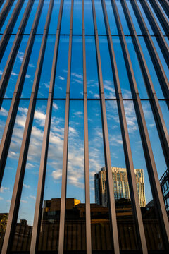 Parallel bars rise past an urban building as vertical lines define the facade, then sky reflection appears across glass while architecture stretches into narrow geometry.