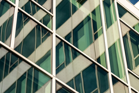 Angled panels cross an urban building in a diagonal grid, breaking the view before green frames meet the facade and windows organize architecture into layered geometry.