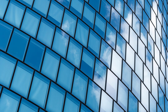 Repeating panels on an urban building follow a curved facade as cloud reflection crosses a blue frame, then glass windows turn architecture into layered geometry.