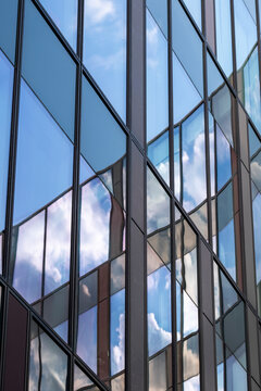 Clouds drift beside a vertical urban building edge as reflection crosses a blue facade under shifting daylight, then glass windows shape architecture into strict geometry.