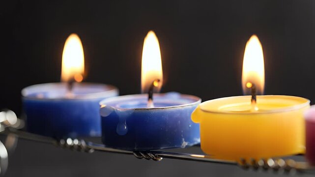 Row of colorful lit candles with a soft glow against a dark background